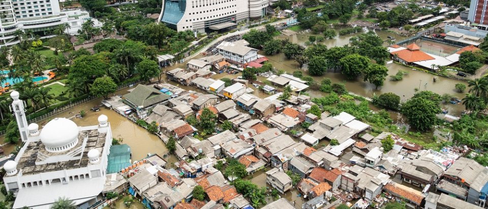 Die überfluteten Straßen in einem armen Wohnbezirk im Herzen der Stadt Jakarta. Daneben moderne Hochhäuser.