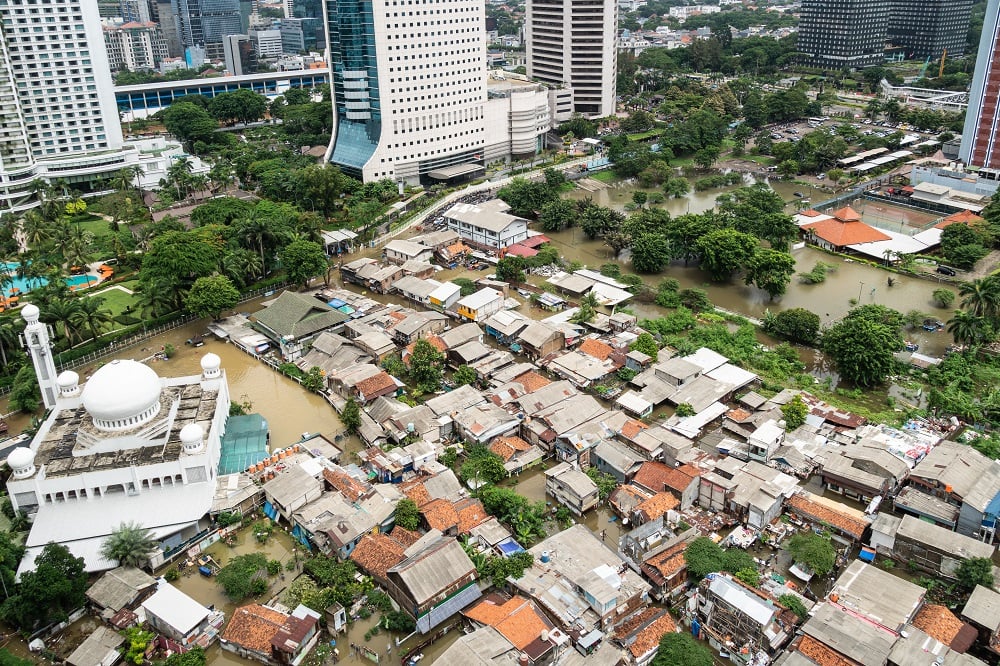 Die überfluteten Straßen in einem armen Wohnbezirk im Herzen der Stadt Jakarta. Daneben moderne Hochhäuser.