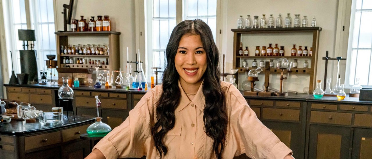 Chemikerin Dr. Mai Thi Nguyen-Kim steht hinter einem Labortisch, auf dem Schüsseln mit brennendem Inhalt und Chemikalien stehen und lächelt in die Kamera. (Foto: ZDF / Maike Simon)