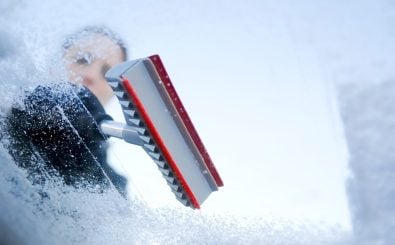 winter driving – scraping ice from a windshield Photo has been taken from the inside of the car. (Foto: trendobjects/shutterstock)