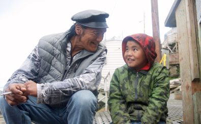Robert Soolook (links) ist Stammesältester auf der Insel Little Diomede. Sein Großneffe Babba rechts) sitzt neben ihm und sie schauen sich lächelnd an. 