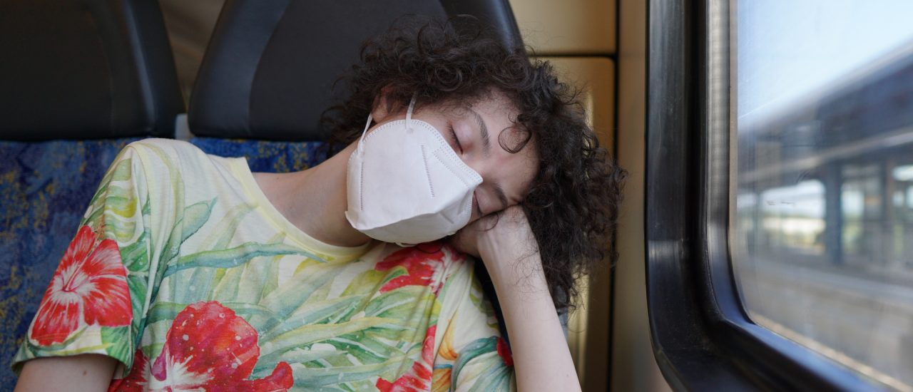 Ein Junge mit Maske schlafend im Zug