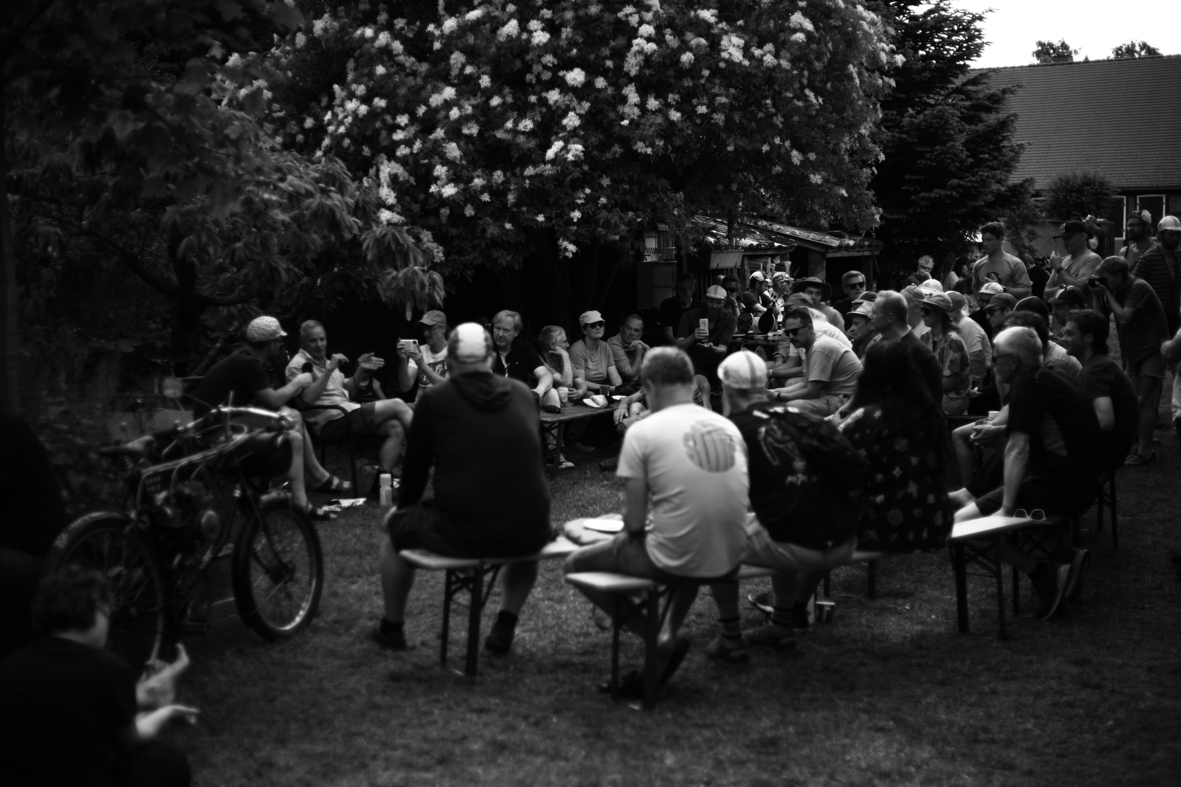 Mehrere Menschen sitzen in einem Garten und hören einer Podcastaufnahme mit dem Rahmenbauer Peter Weigle zu