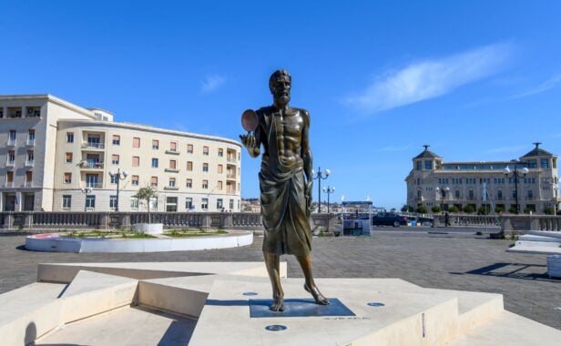 SYRACUSE, ITALIEN – 20. APRIL 2025: Die Bronzestatue des antiken griechischen Mathematikers Archimedes, der einen brennenden Spiegel hält, befindet sich am Eingang zur Insel Ortygia, Sizilien. Foto: Mitzo / Shutterstock.com