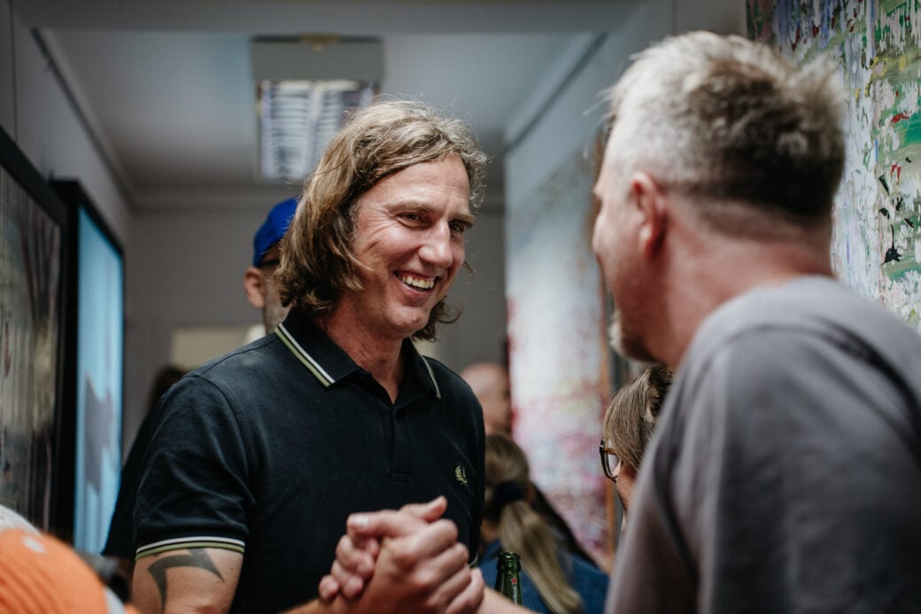 Ein lächelnder Mann mit langen Haaren begrüßt einen Besucher des Ateliers HeARTattack mit Handschlag. Foto: oliverfreund_fotografie